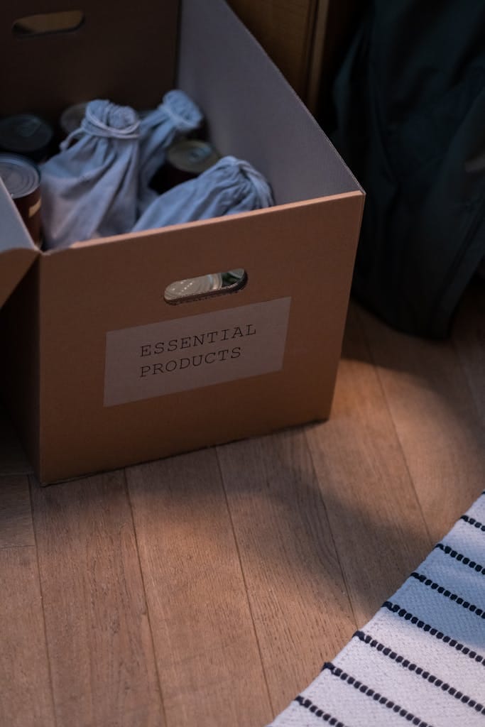 Cardboard box labeled 'Essential Products' filled with goods on wooden floor.